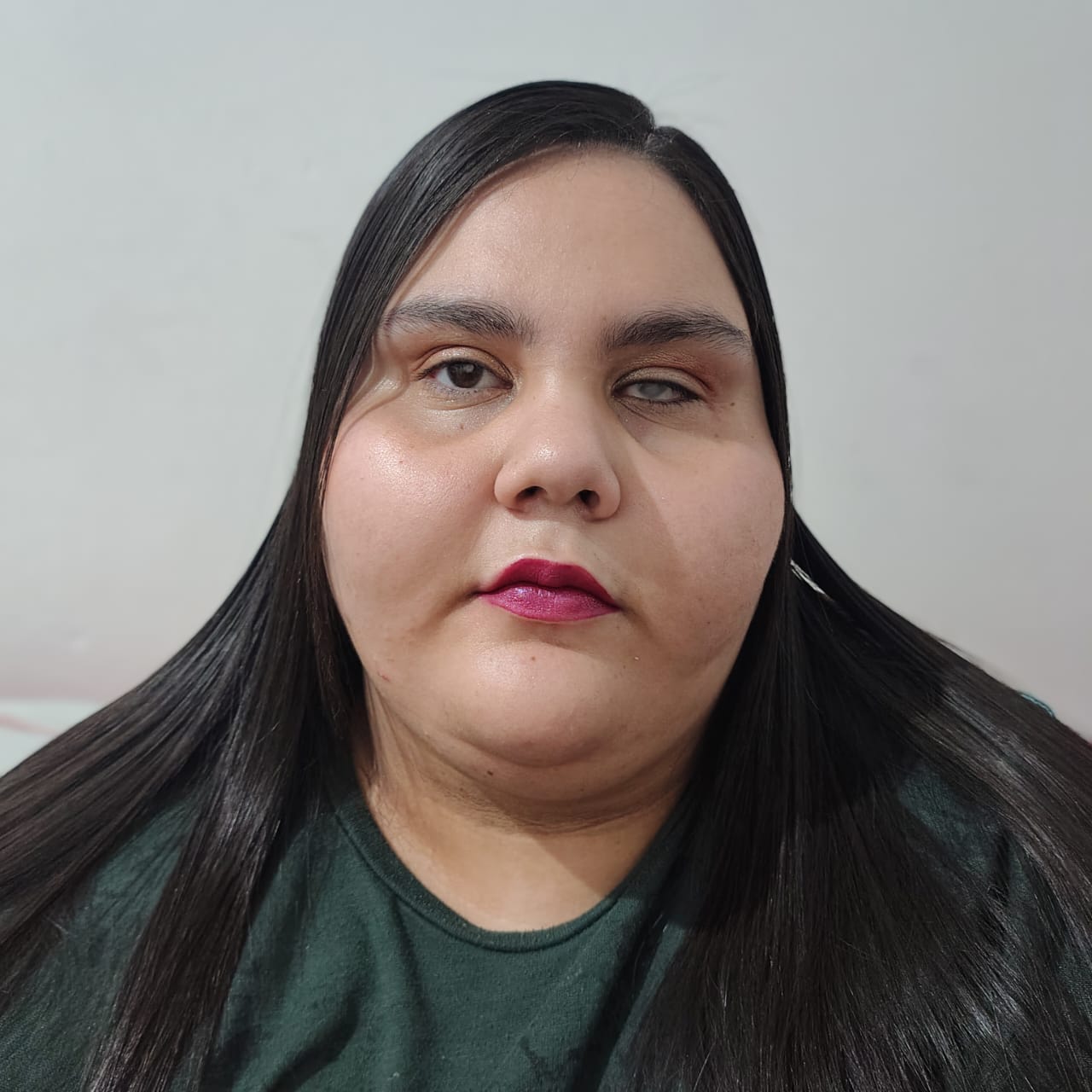 Beatriz Fernandes Bezerra com cabelo liso e longo, batom magenta e blusa verde escura diante de fundo claro