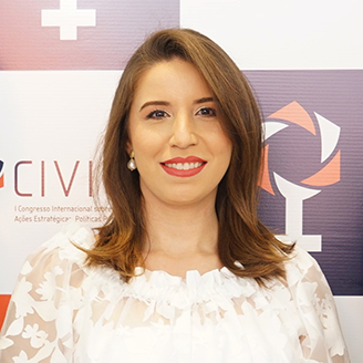 Sílvia Rebeca Sabóia Quezado com cabelo castanho claro nos ombros, batom vermelho e blusa branca rendada diante de painel com logotipos
